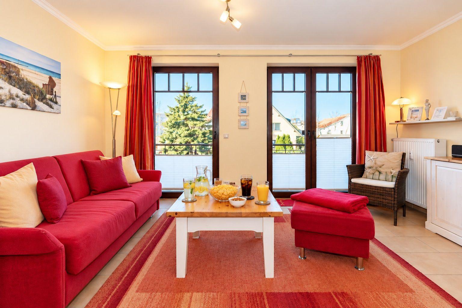 Ein Wohnzimmer mit rotem Sofa, Holztisch und Blick auf Balkon.