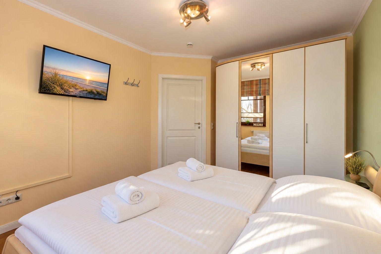 Schlafzimmer mit Doppelbett, Kleiderschrank und Wandfernseher.