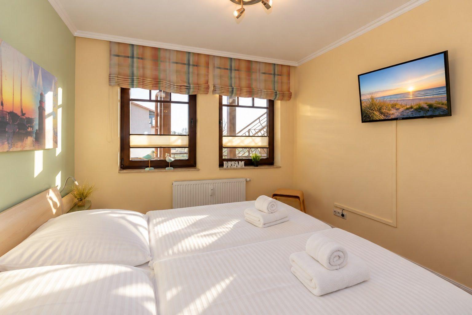 Schlafzimmer mit Doppelbett, Fenster, Fernseher und Wandbild.