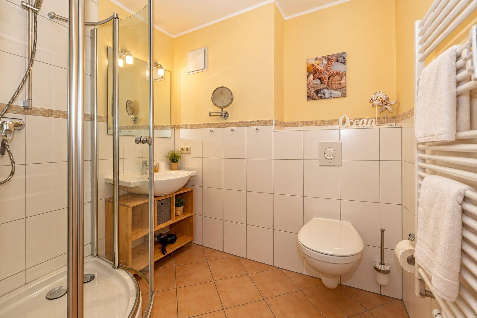 Badezimmer mit Dusche, Waschbecken und Toilette. Wandbild mit Meeresmotiv.