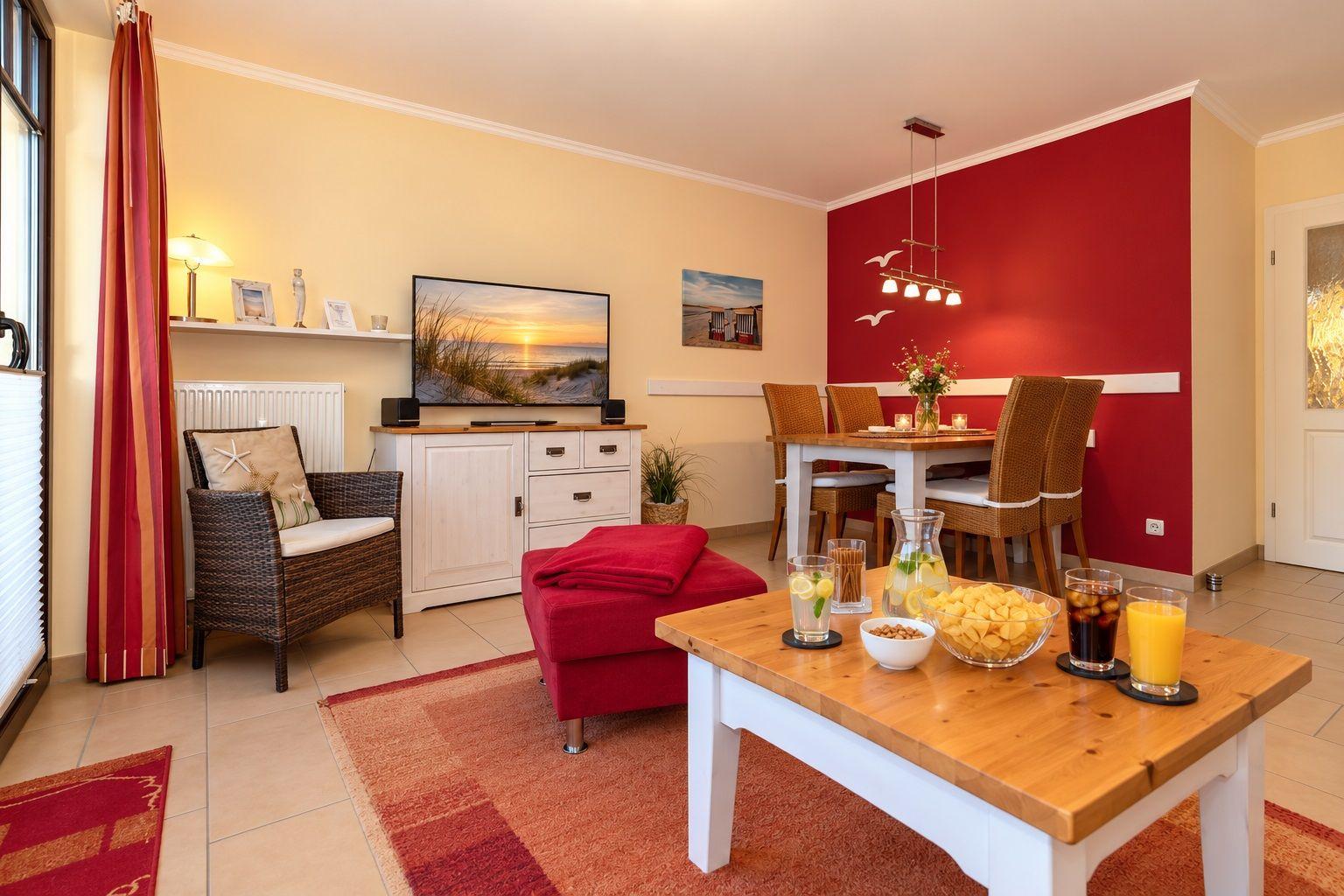Wohn- und Essbereich mit roter Wand, TV, Esstisch und Sitzgelegenheiten.