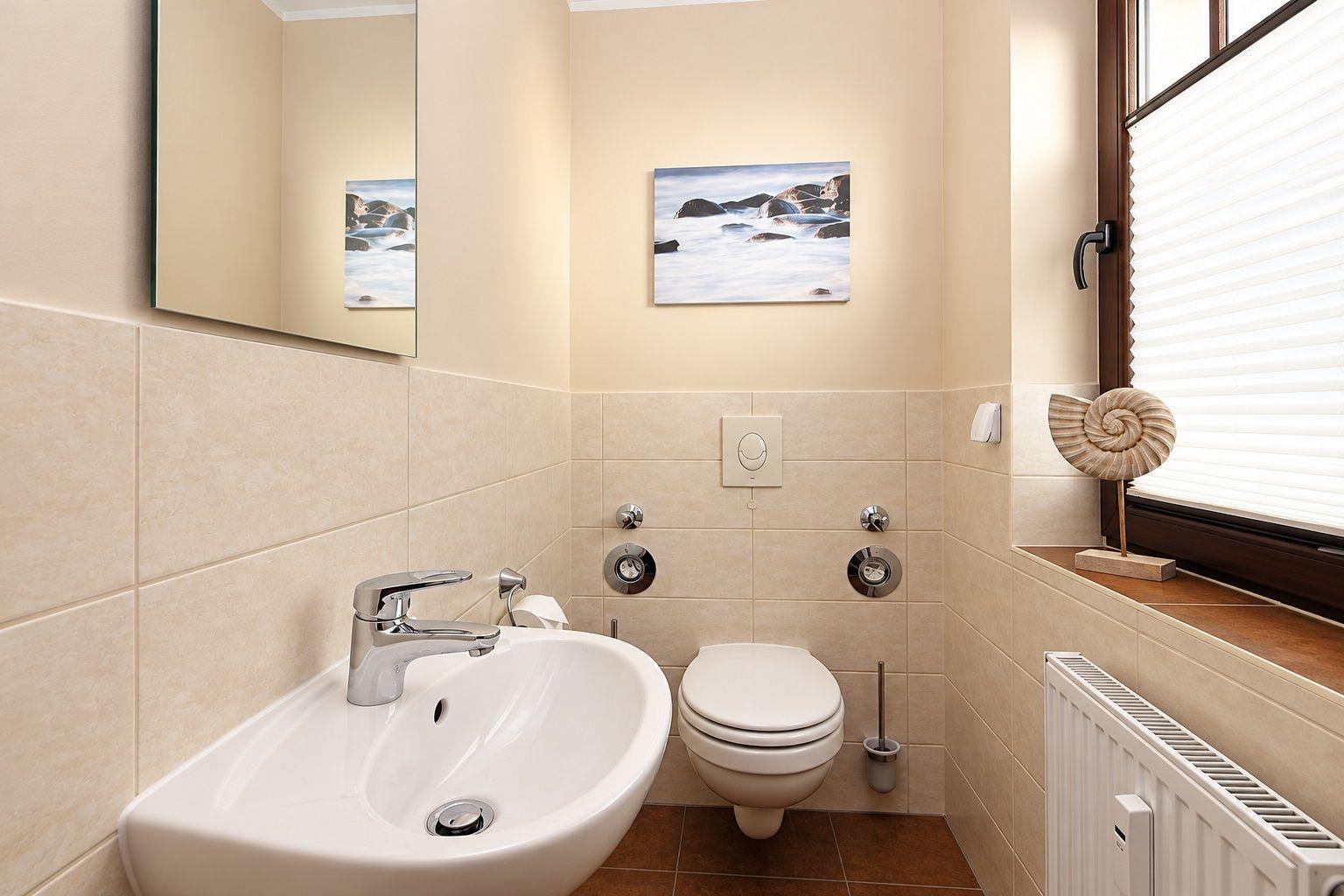 Badezimmer mit Waschbecken, Toilette und Fenster mit Muscheldekoration.