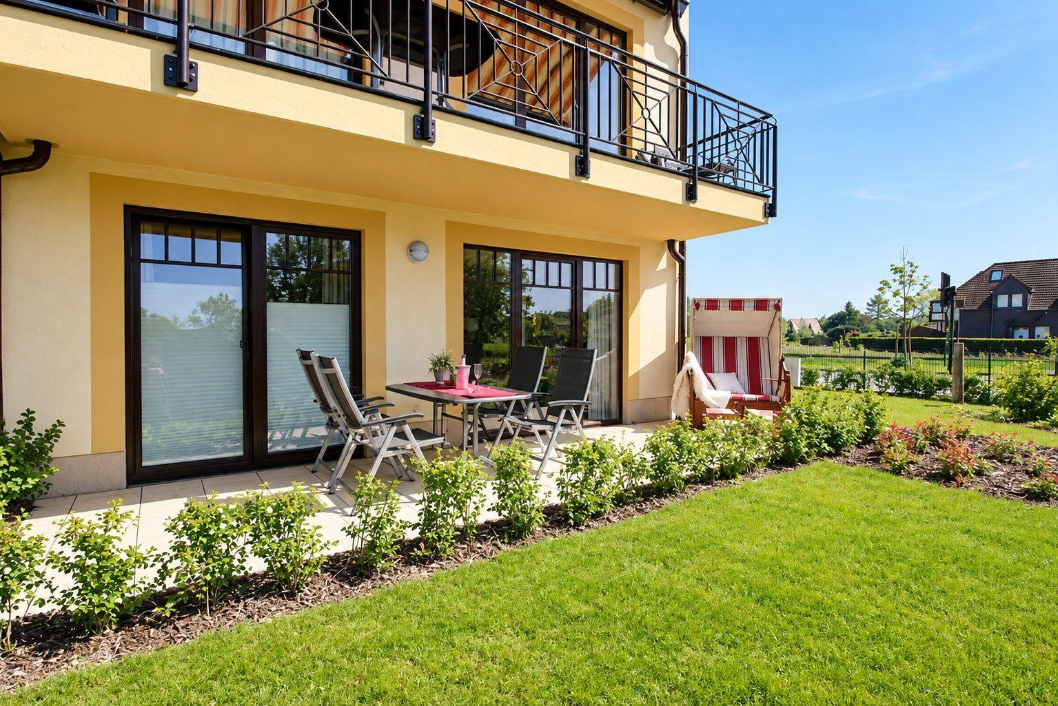 Terrasse mit Tisch, Stühlen und Liegestuhl. Hinterhof mit Rasen und Beerensträuchern.