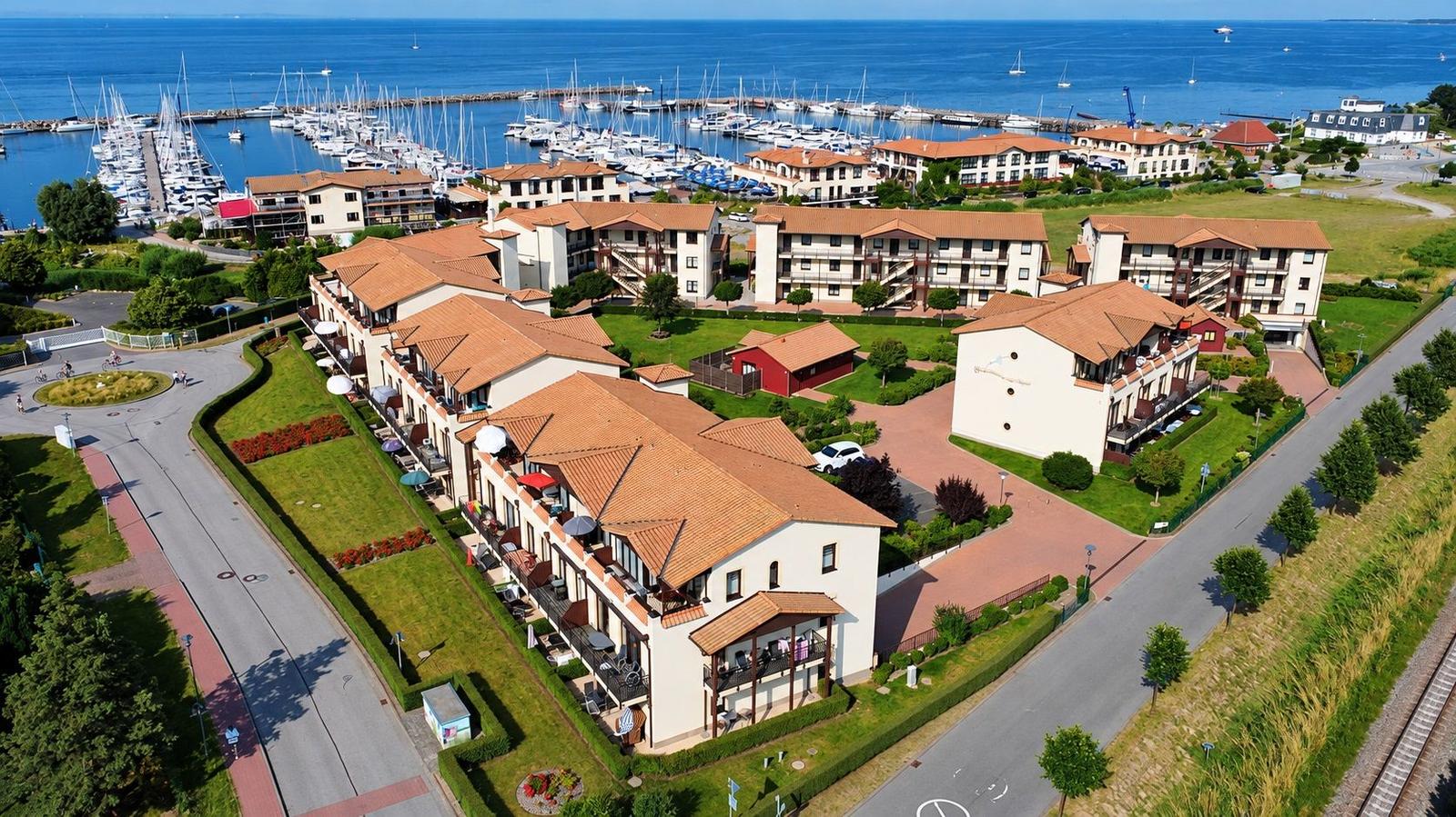 Häuserkomplex mit Terrassen und Blick auf Hafen mit Booten.