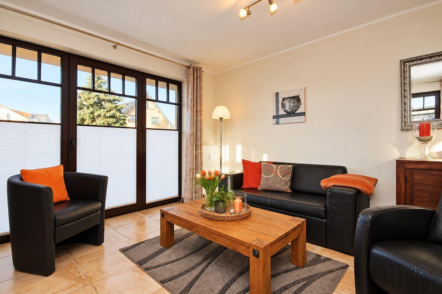 Wohnzimmer mit Sofa, Sessel und Holztisch. Große Fenster, Wandbild und Spiegel.
