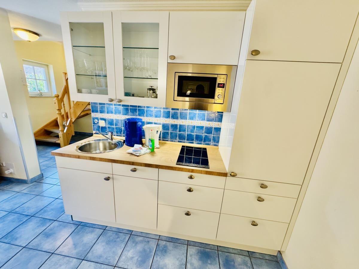Essbereich mit Holztisch, Stühlen und Küchenbereich im Hintergrund.