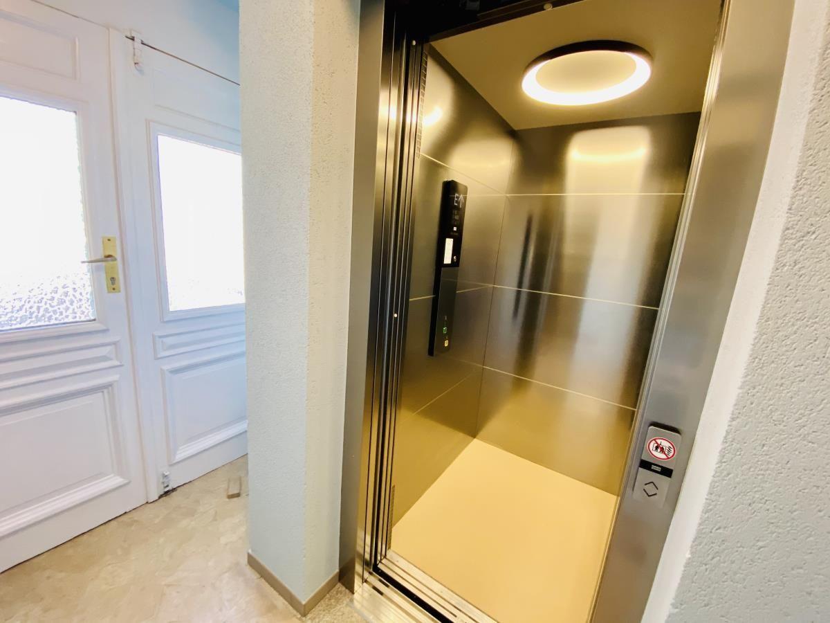 Weißer Bank am gepflasterten Platz vor Wohnhaus mit rotem Dach und Parkplatz.
