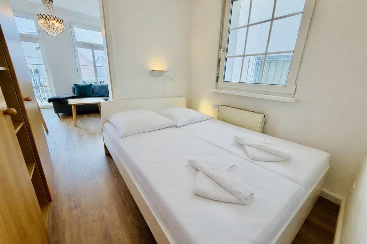 Schlafzimmer mit Bett, Holzregal und Fenster. Wandbild zeigt Sonnenblumen.