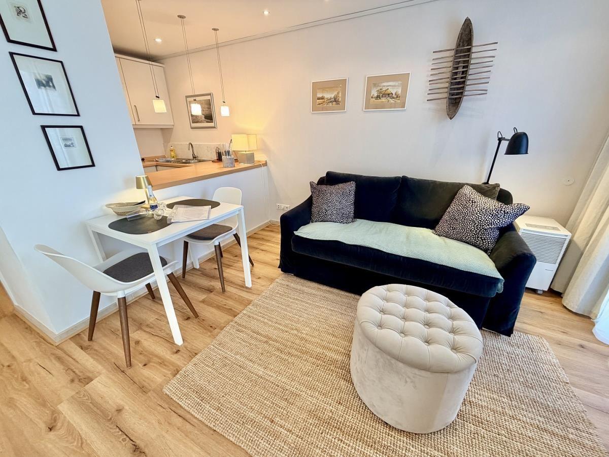 Schlafzimmer mit Bett, Wohnbereich mit Sofa und Essplatz, weiße Wände und Holzboden.