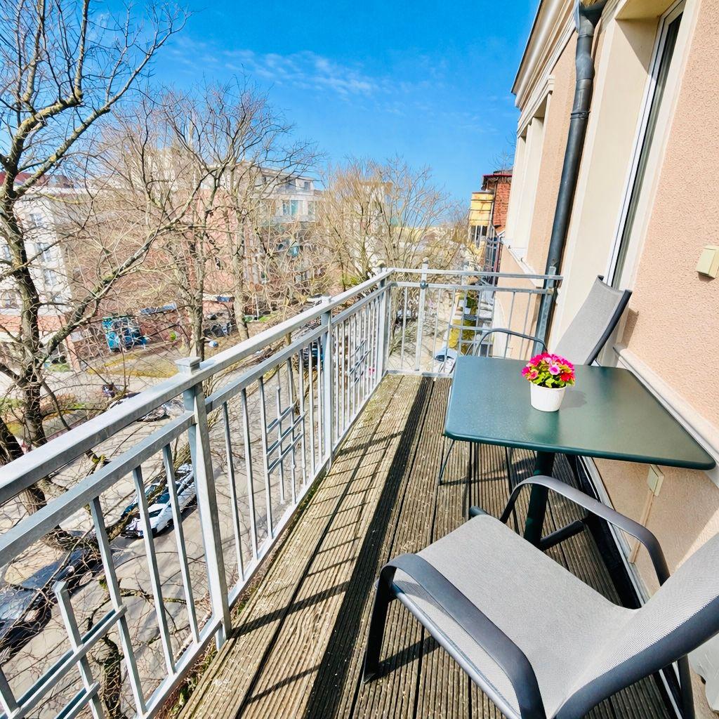 Wohnzimmer mit blauem Sofa, weißem Sessel und Holzboden. Zwei Fenster und TV-Möbel.