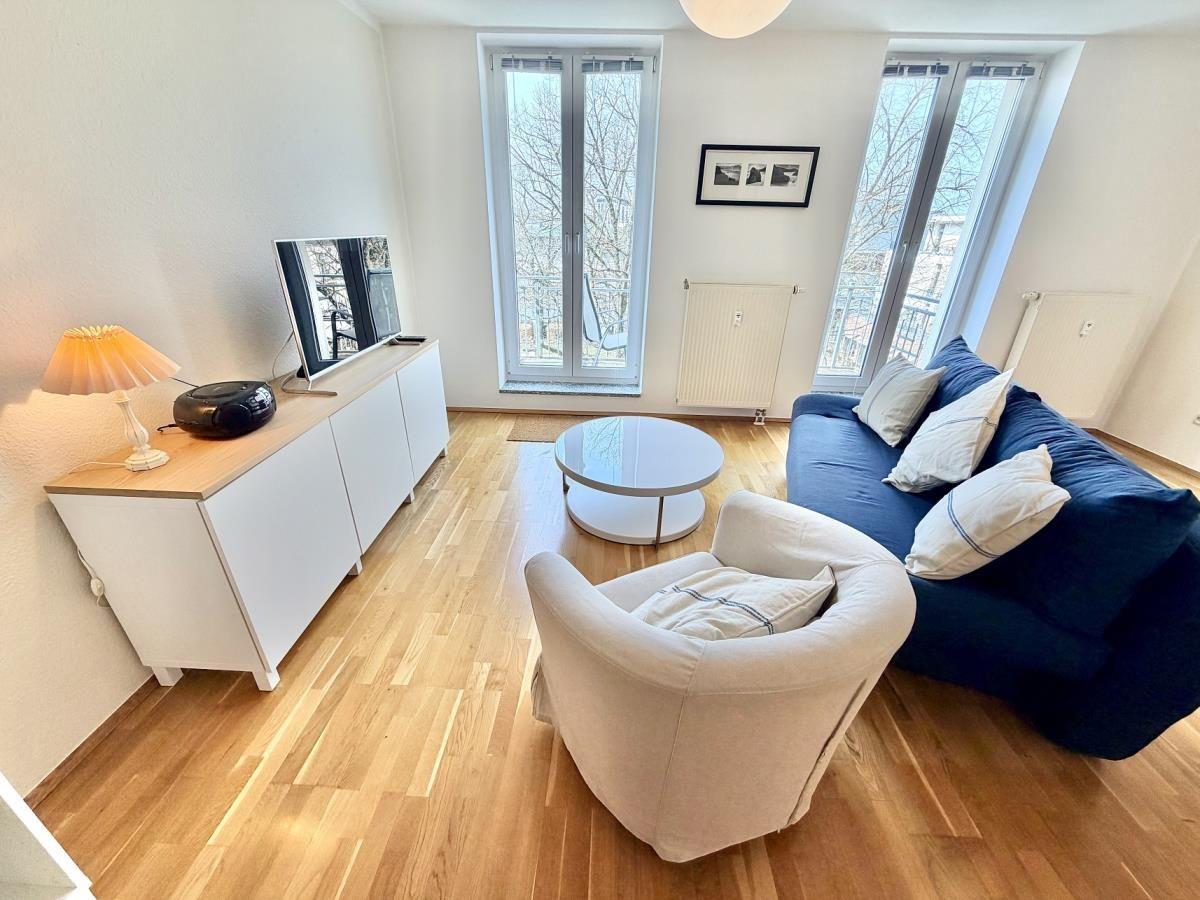 Wohnzimmer mit blauem Sofa, runden Tisch und Küchenbereich im Hintergrund.