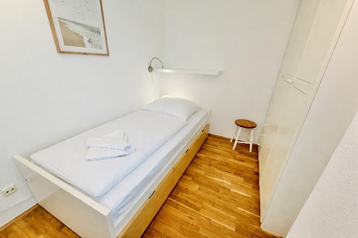 Zwei Einzelbetten mit weißen Laken, dunkler Sessel und Holzboden.