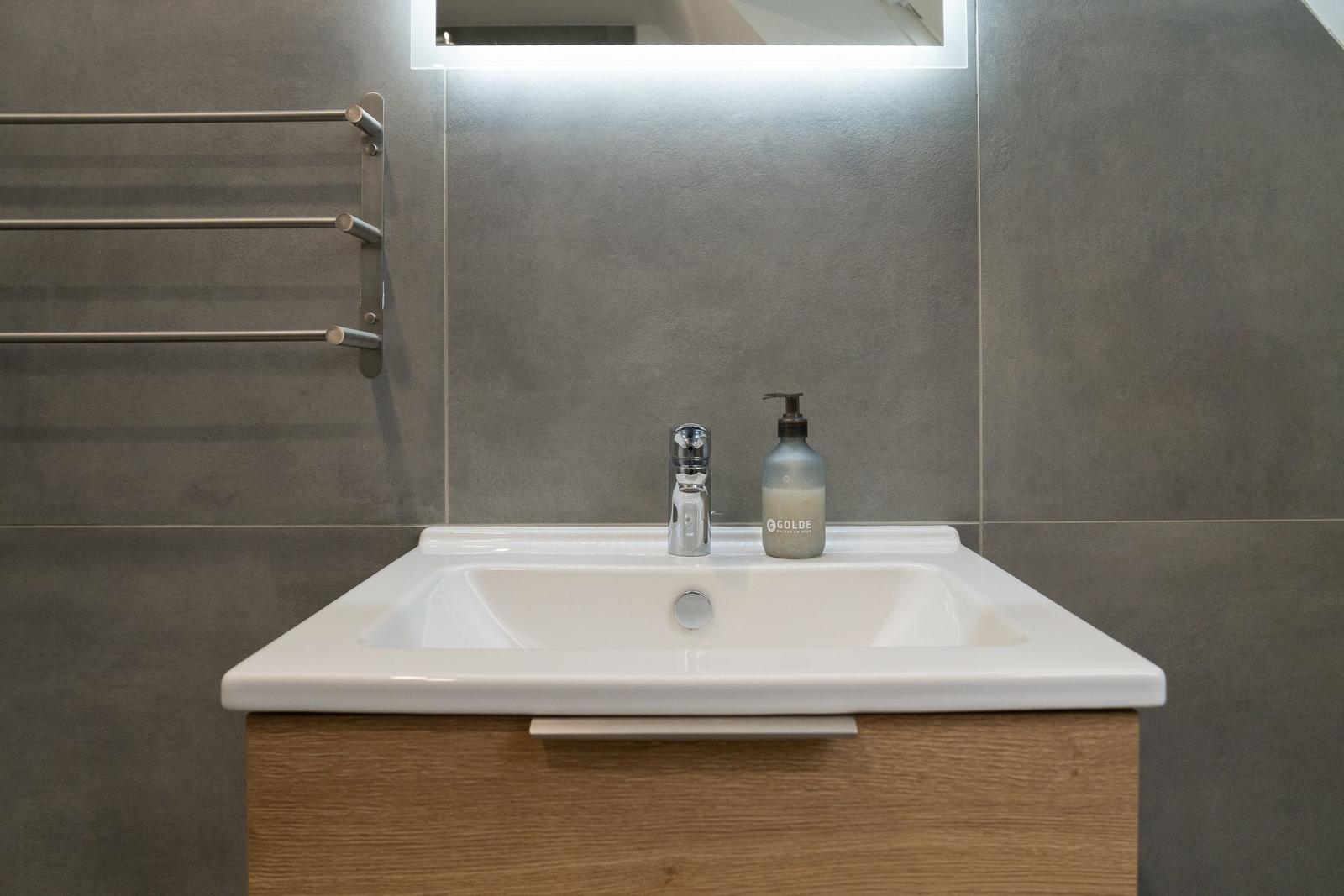 Waschbecken mit Spiegel und Handtuchhalter an grauer Wand