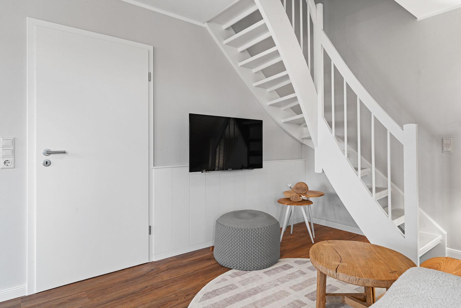 Wohnbereich mit weißer Treppe, Fernseher und Holzmöbeln.