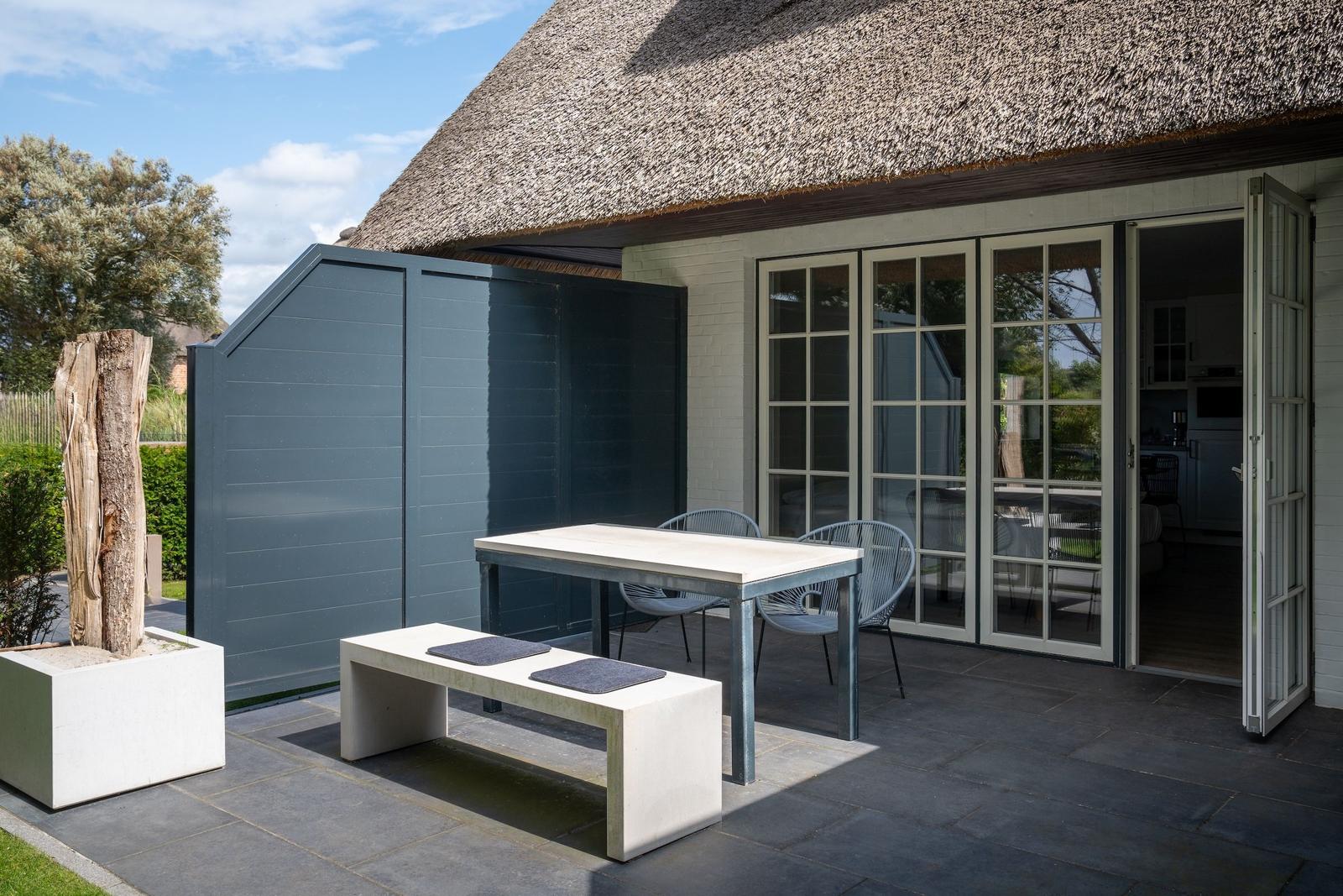 Terrasse mit Tisch, Bänken und Sicht auf das Haus mit Strohdach.