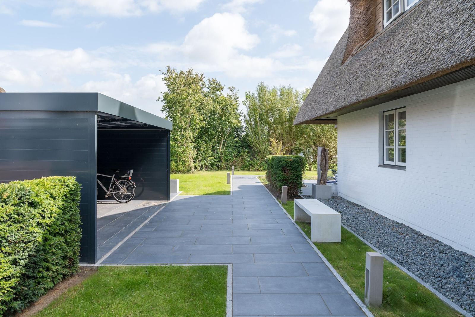 Pflasterweg führt zu einem Haus mit Strohdach und moderner Garage mit Fahrrad.