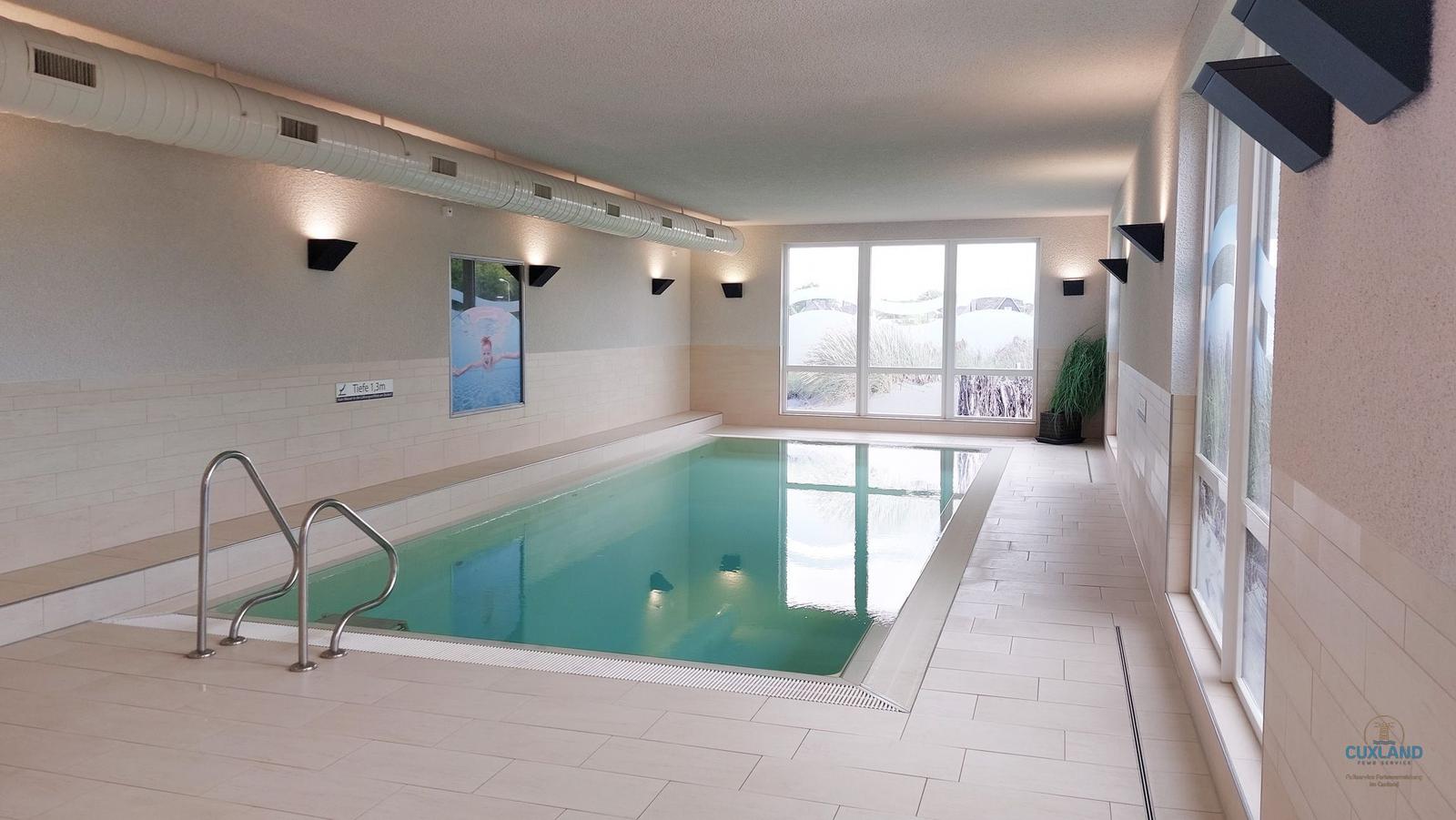 Innere Schwimmhalle mit blauen Liegestühlen und großflächigen Fenstern.