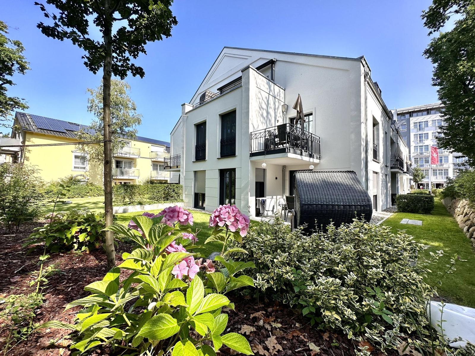 Villa Sofie mit Balkon, Eingang und Garagenzugang. Modernes Gebäude mit Pflanzenbeeten.