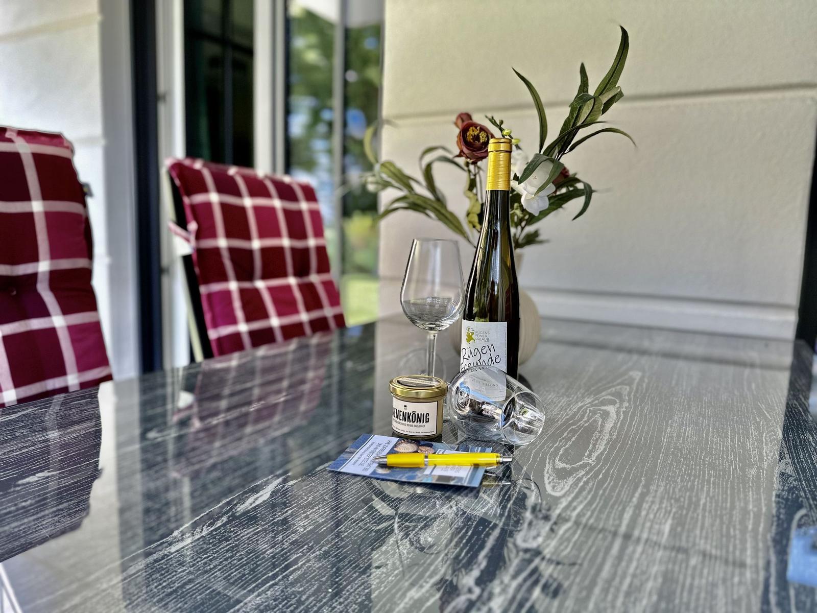 Terrasse mit Sonnenschirm, Tisch und Stühlen. Hintergrund: grüner Garten und gelbes Haus.