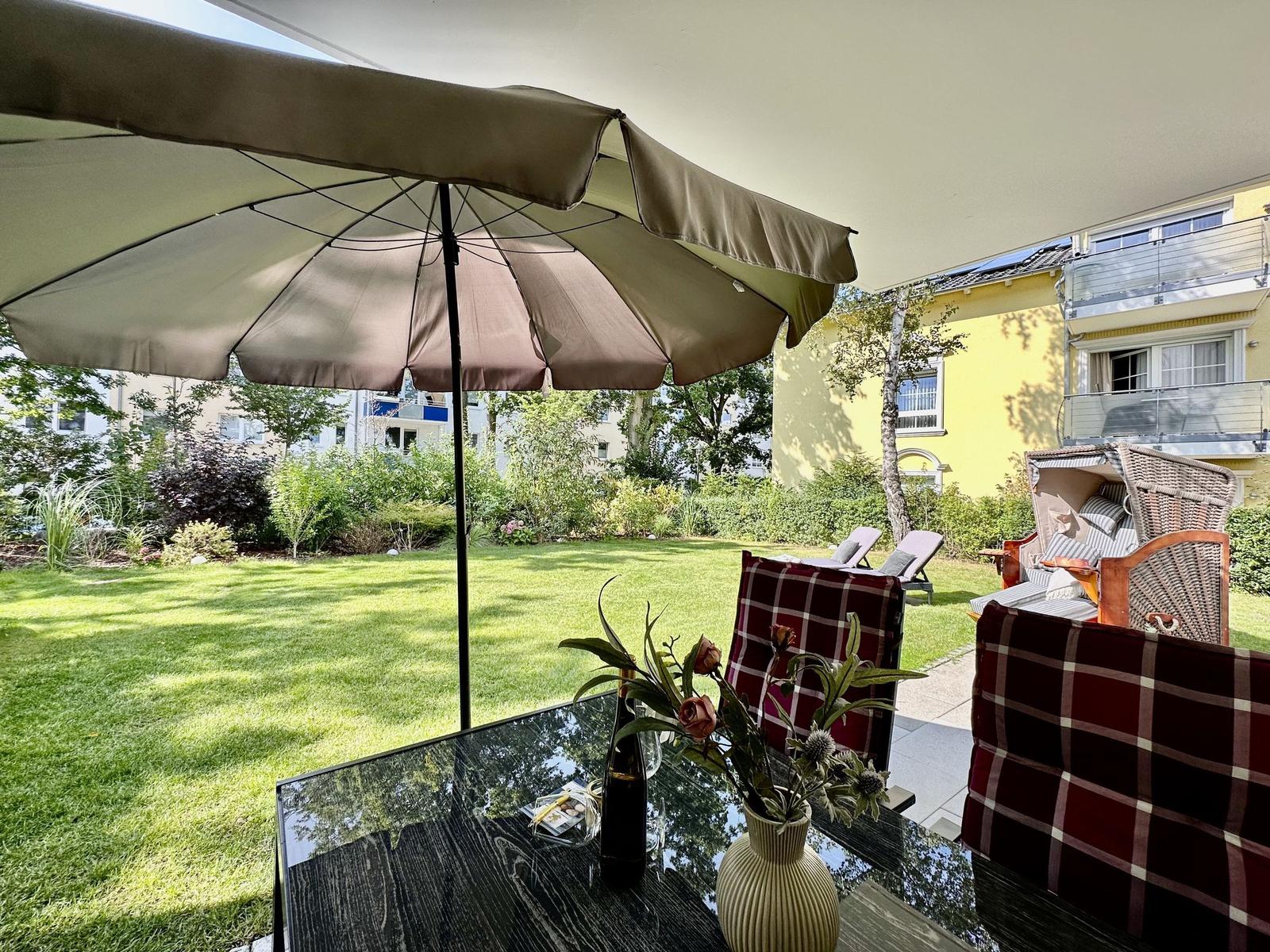 Moderne weiße Villa mit Balkonen und Garten. Gartenmöbel und Sonnenschutz sind vorhanden.