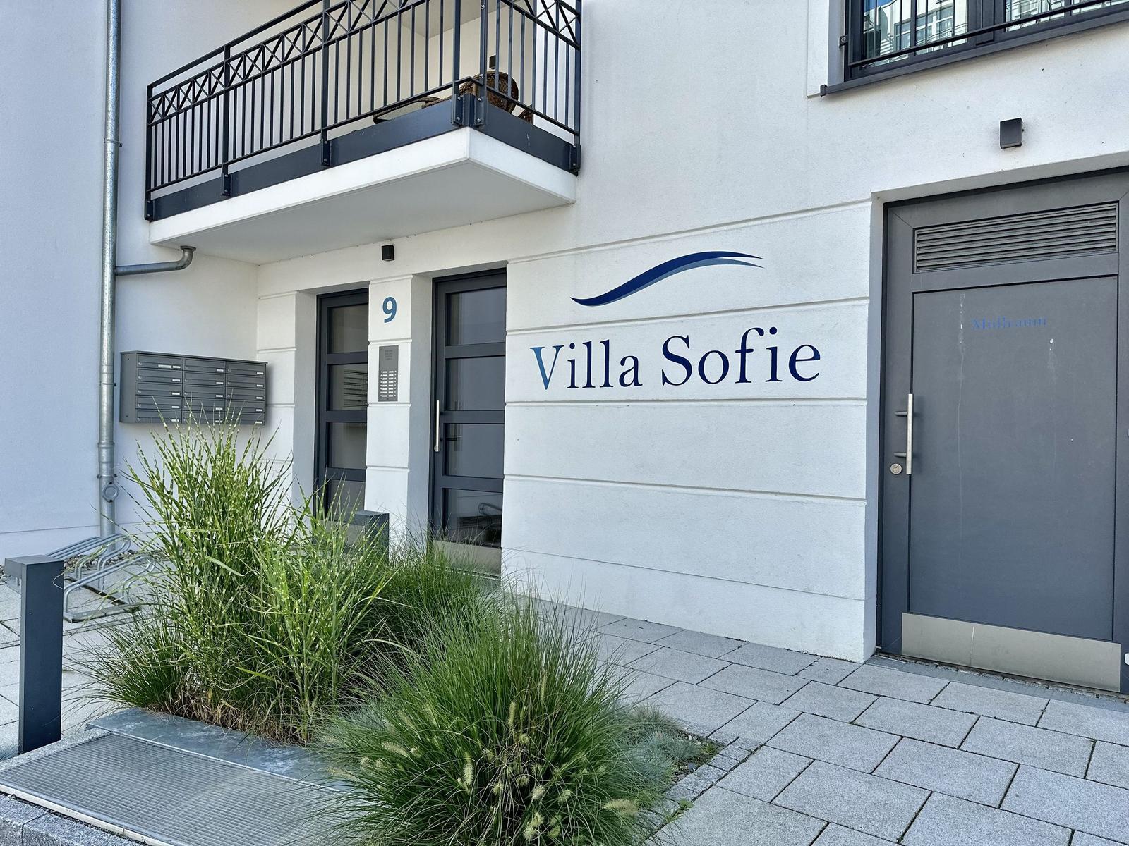 Weißes Mehrfamilienhaus mit Balkonen und Garten. Villa Sofie an der Straße.