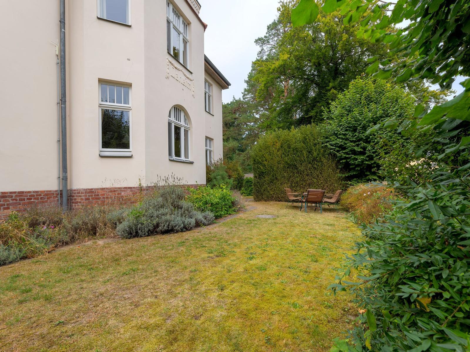 Hinterhof mit Tisch und Stühlen, umgeben von Grünflächen und Sträuchern.