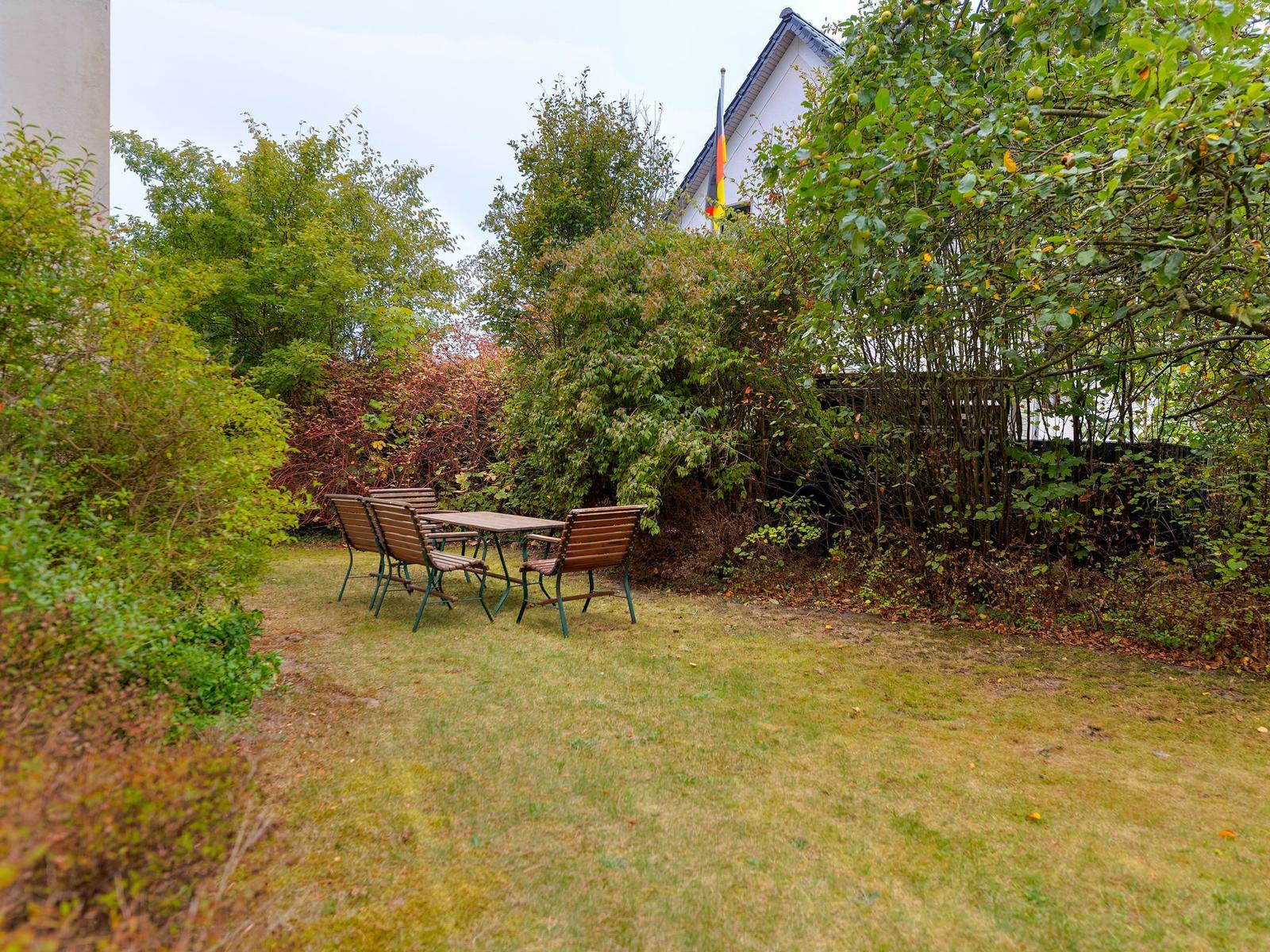 Hinterhof mit Tisch, Stühlen und Sitzbank. Grünflächen und Bäume umgeben den Außenbereich.