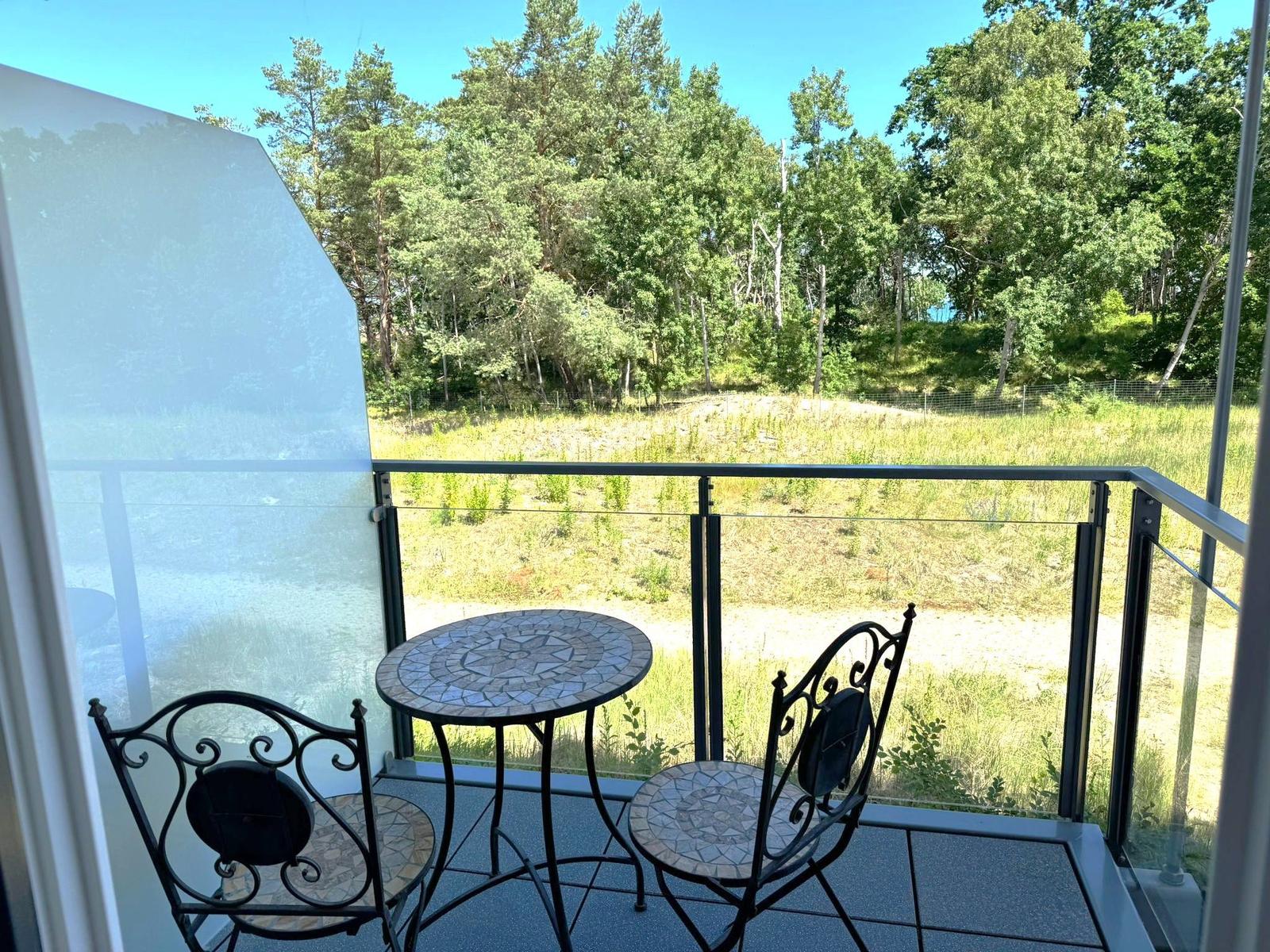 Terrasse mit Tisch und zwei Stühlen, Blick auf Wald und Grasland.