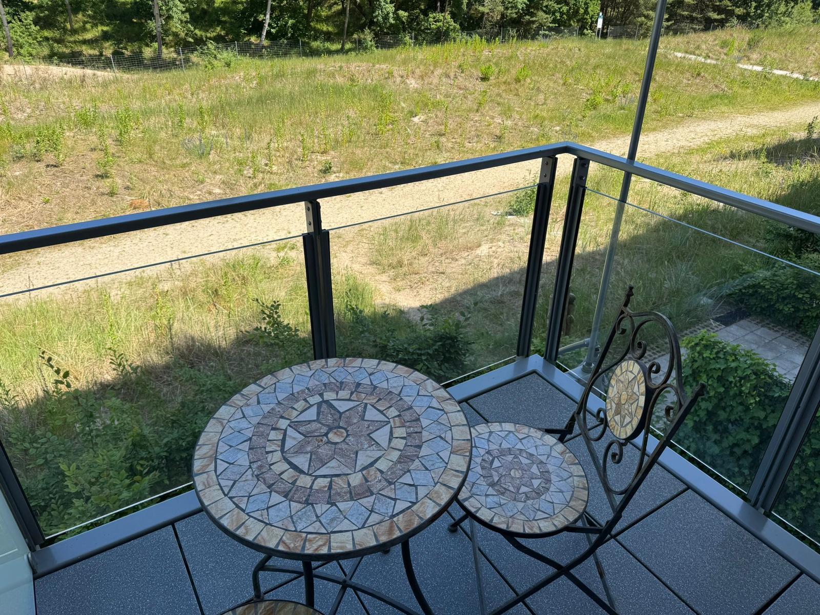 Balcony with mosaic table and chair, overlooking grassy field and trees.