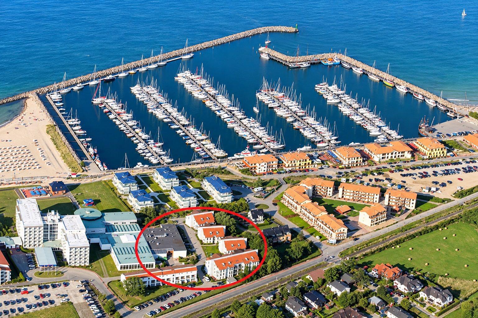 Wohnhaus mit Balkonen und Parkplatz an der Küste mit Yachten im Hintergrund.