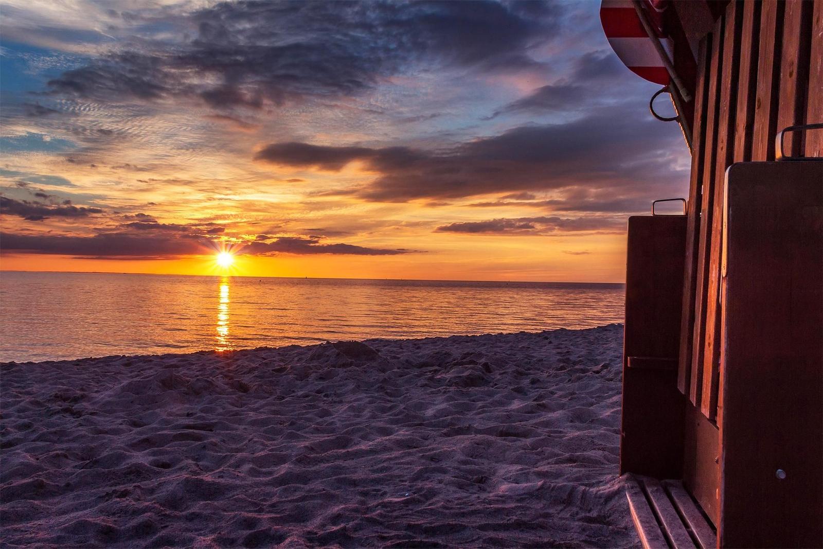 Gruppe am Strand bei Sonnenuntergang um Lagerfeuer versammelt.