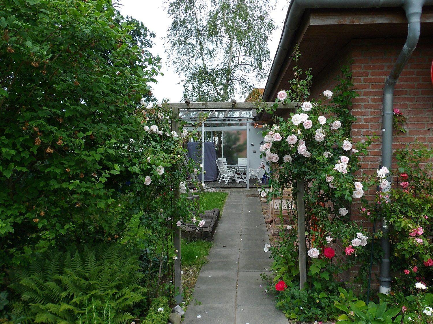 Terrasse mit Tisch, Stühlen und Hängestuhl. Garten mit Blumen und Gras.