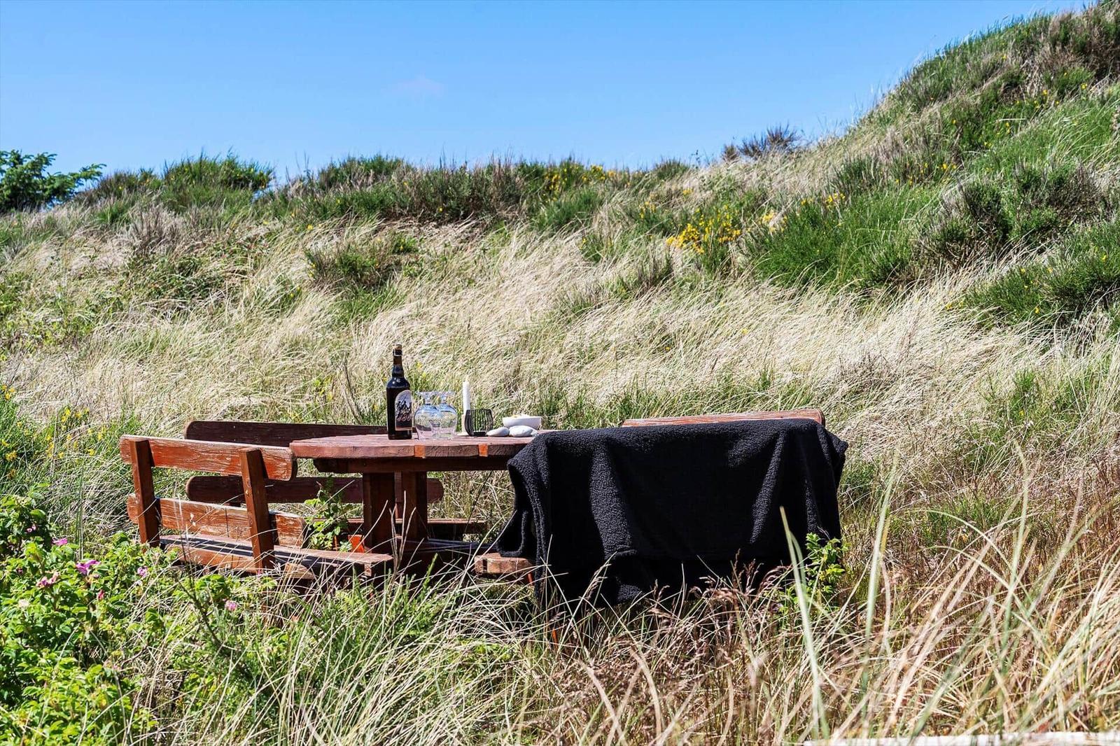 Holztisch mit Gästebuch, Tasse und Puzzle. Blick auf grüne Dünen unter blauem Himmel.