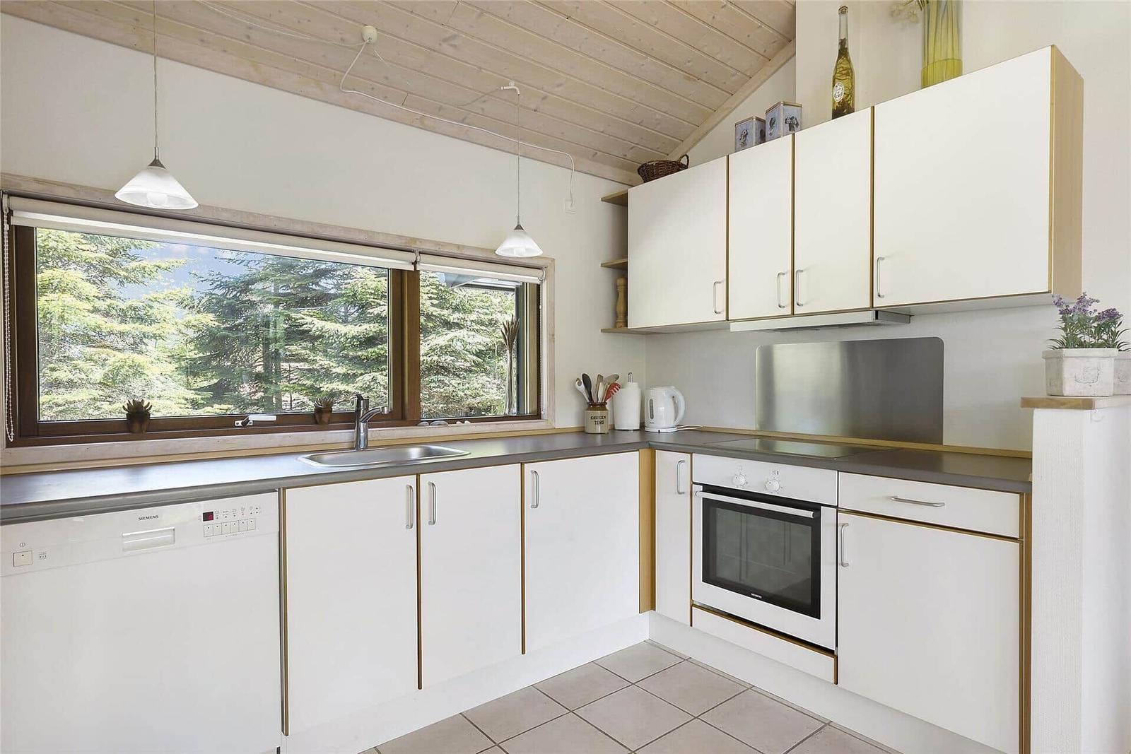 Wohnzimmer mit Sofa, Couchtisch und Kamin. Große Fenster bieten Blick auf Wald.