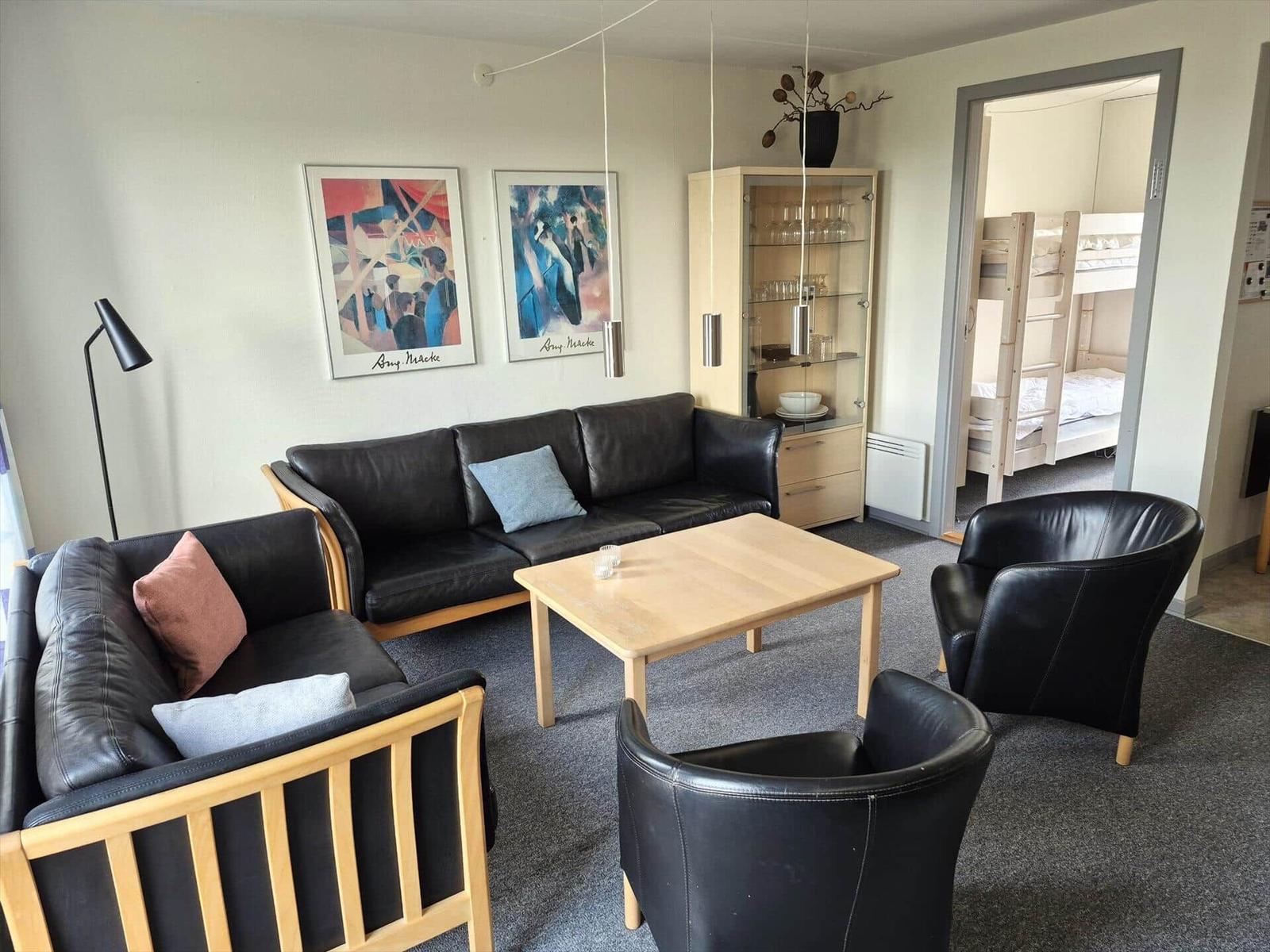 Wohnzimmer mit zwei Sofas, zwei Sesseln und einem Tisch. An den Wänden hängen Bilder.