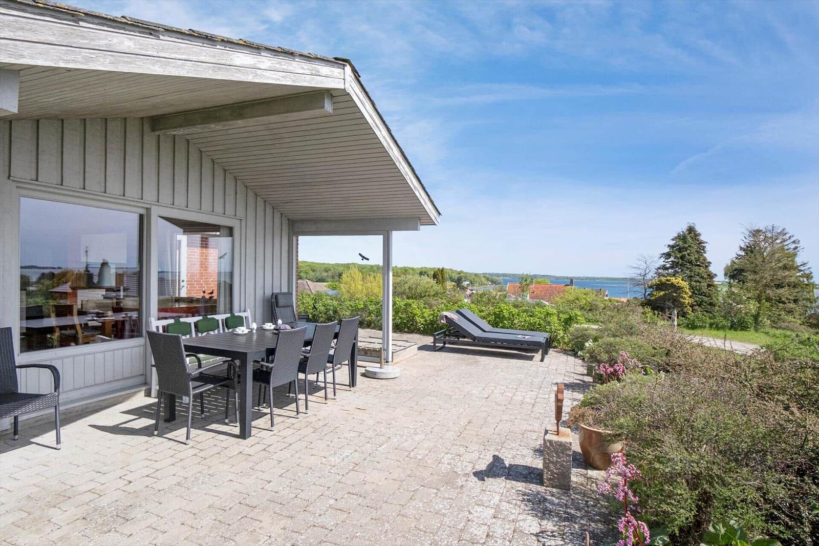 Terrasse mit Tisch und Stühlen, Blick auf Grünfläche und Baum.