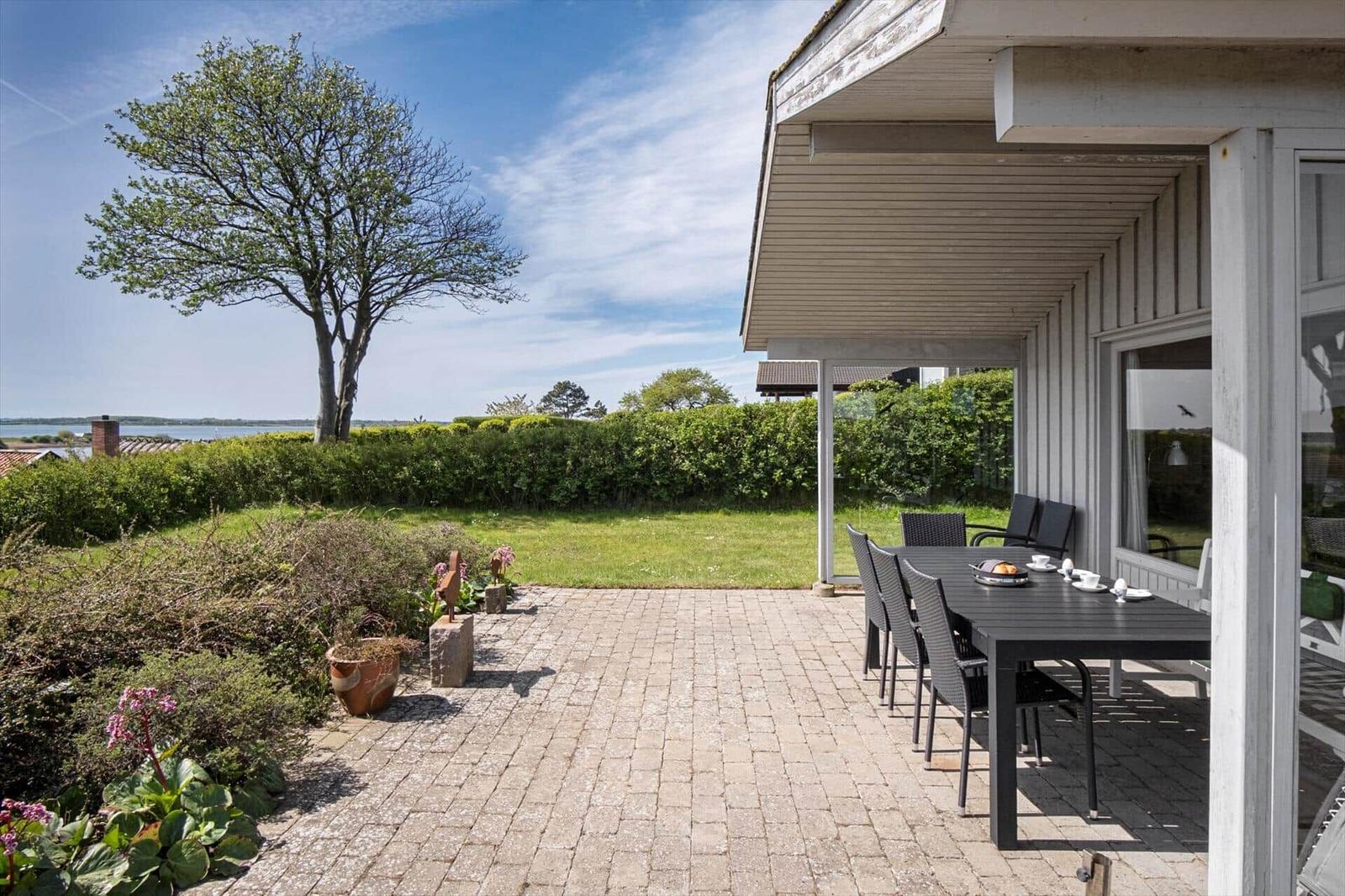 Terrasse mit Tisch, Stühlen und Blick auf Wasser und Grün.