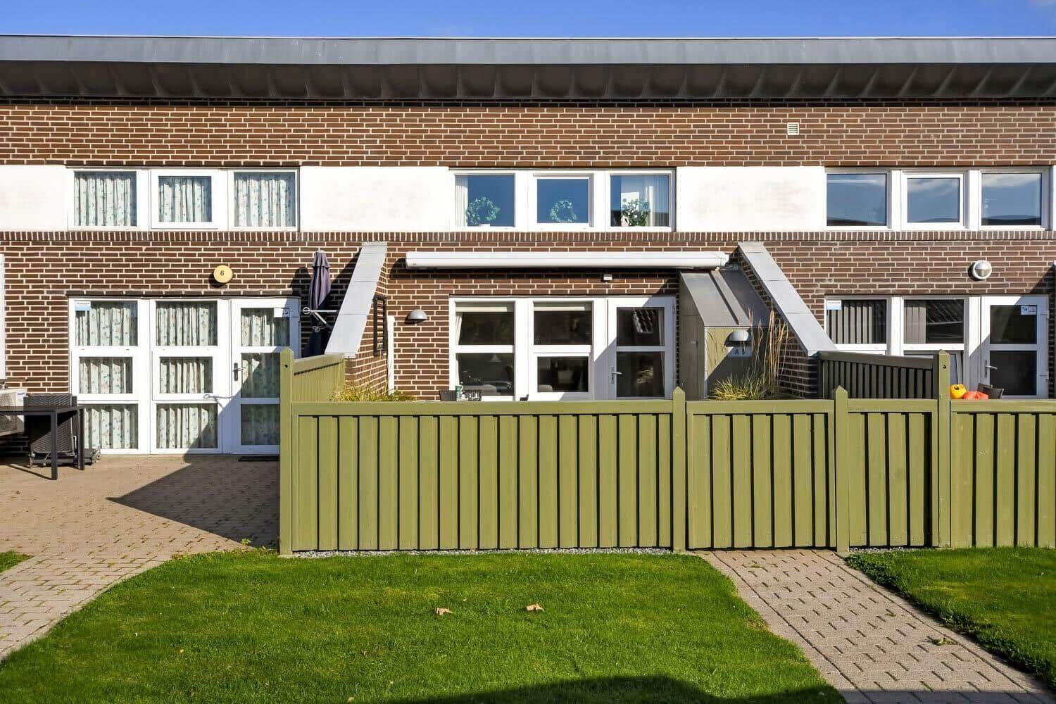 Play area with sandbox, swing, and slide in front of a brick building.