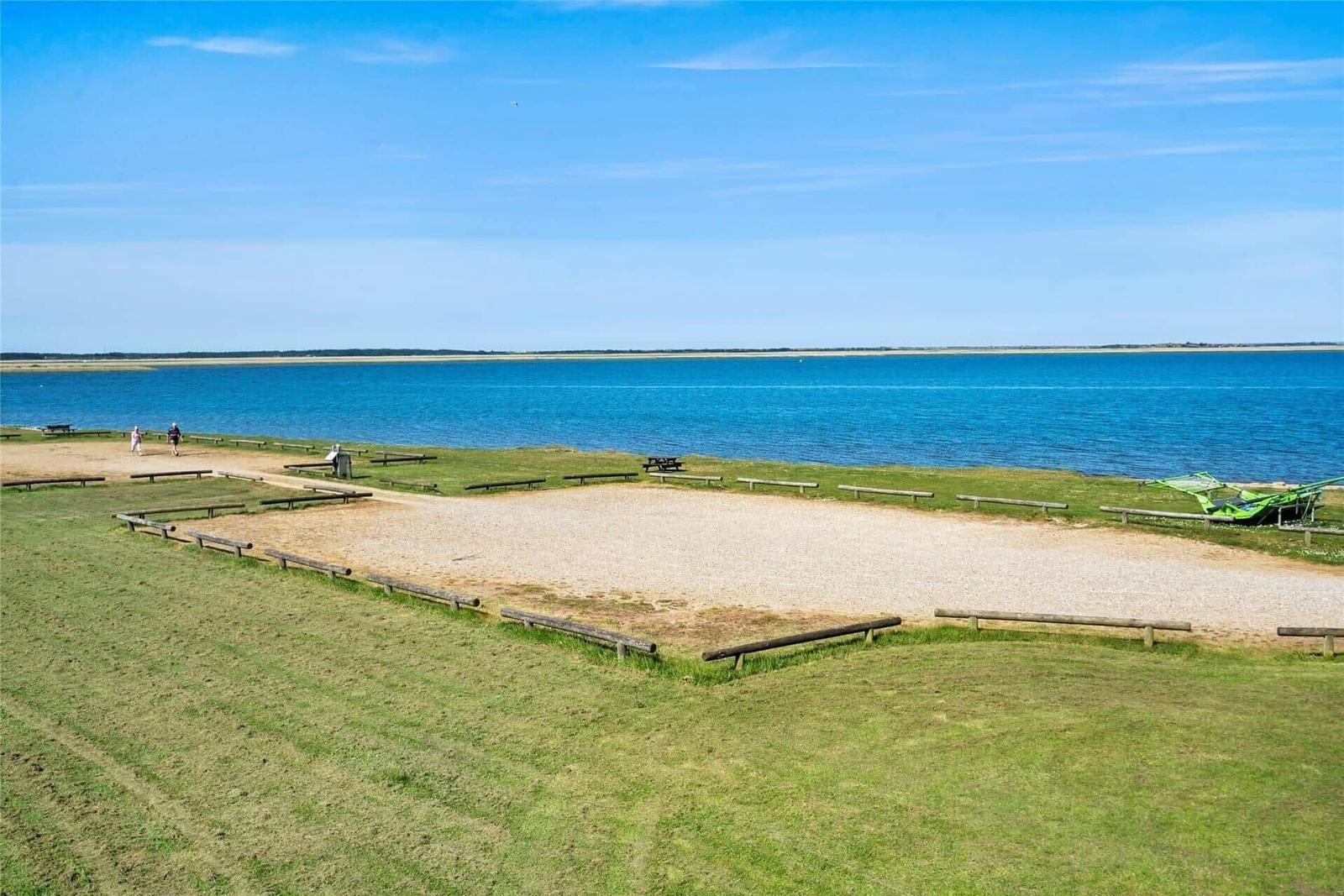 Grassy slope with pier and view of blue water. Wooden railings and picnic tables.