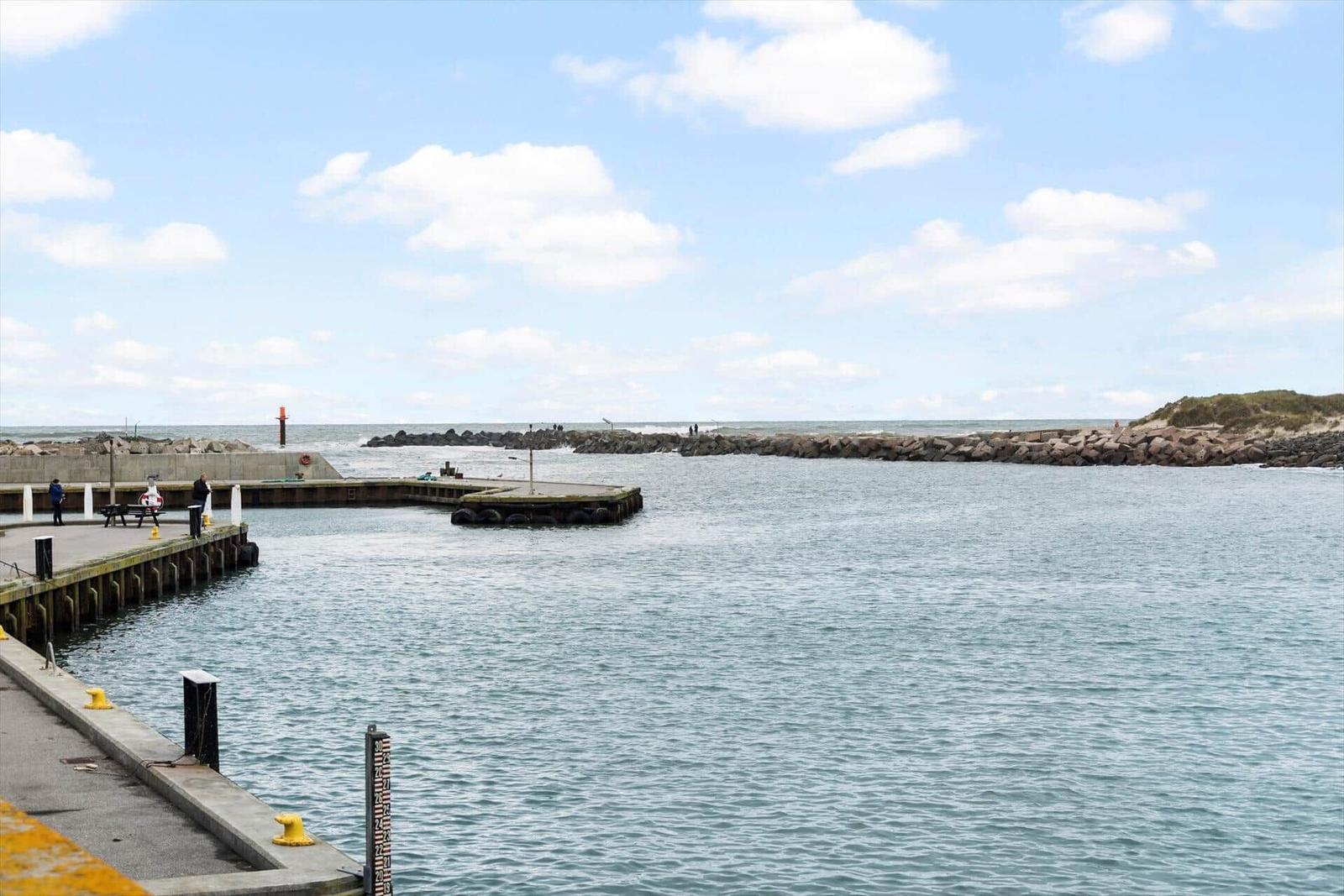 Hafen mit Steg, Steinen und ruhigem Wasser unter blauem Himmel.