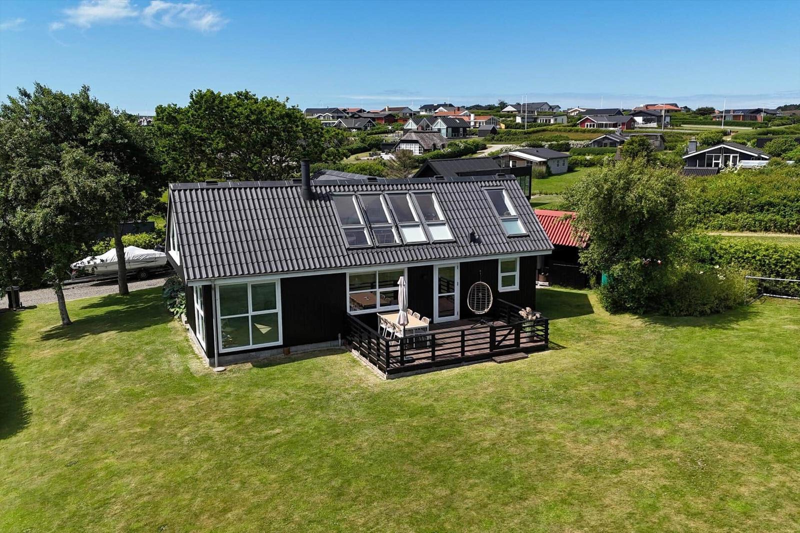 Schwarzes Haus mit Terrasse, umgeben von Grün und Blick auf das Meer.