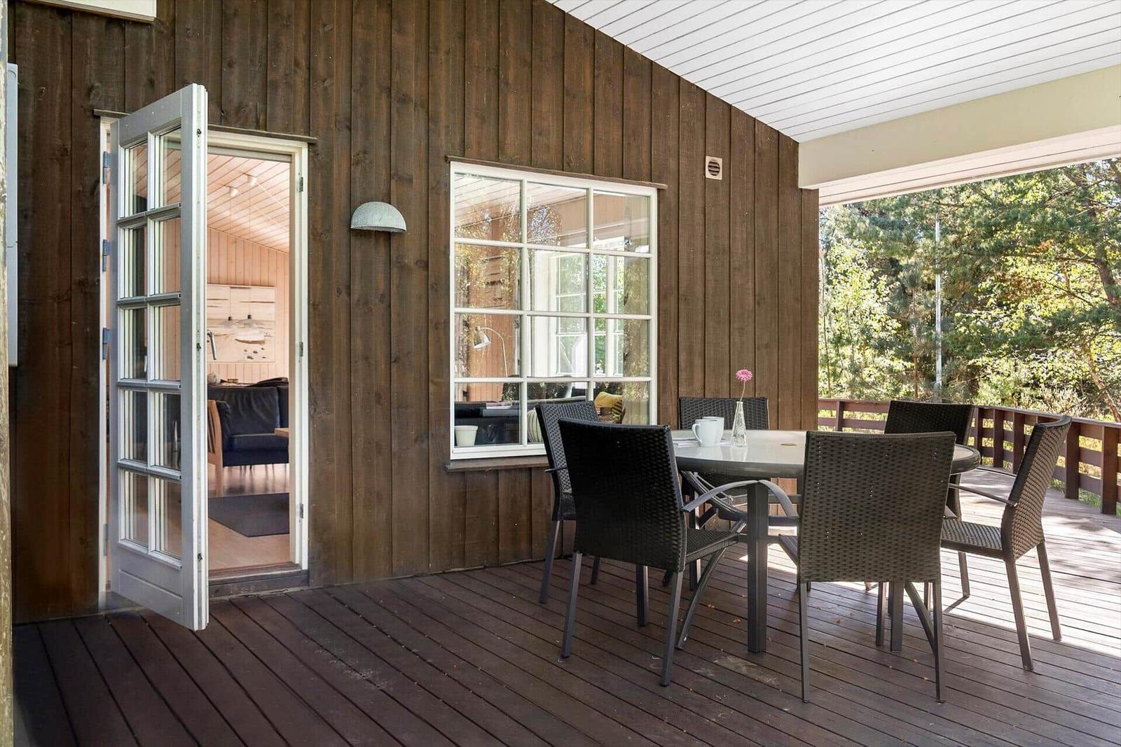 Holzterrasse mit Picknicktisch und Liegestühlen vor einem Holzhaus im Wald.