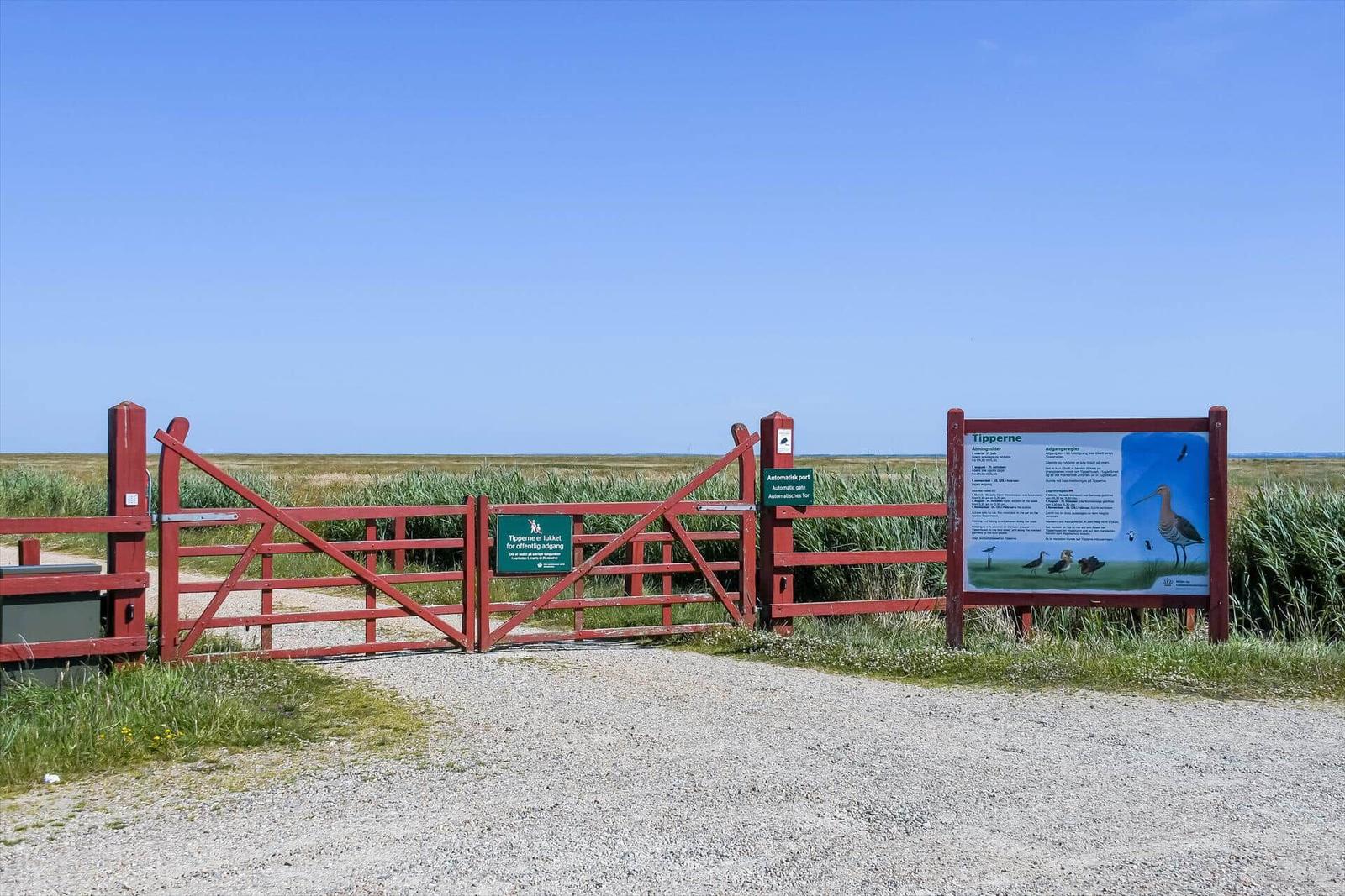 Roter Torbereich mit Informationstafel in Graslandschaft unter blauem Himmel.