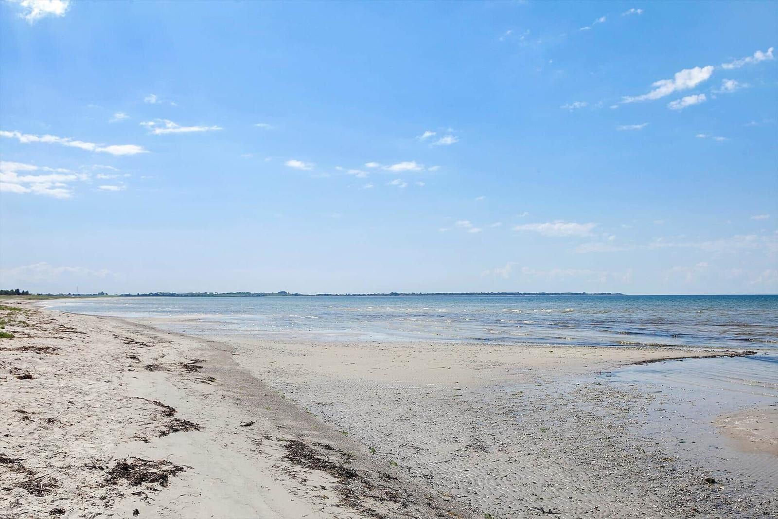 Strand mit Sand und Wasser unter blauem Himmel mit weißen Wolken.