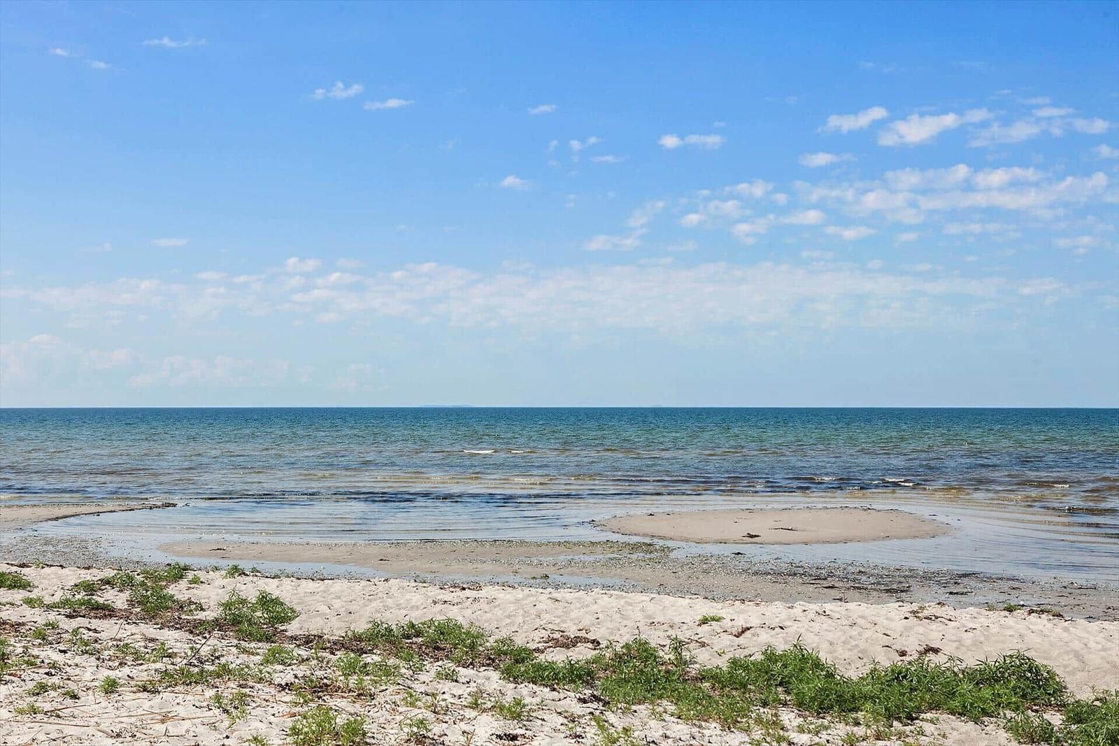 Strand mit Sand und Wasser unter blauem Himmel mit weißen Wolken.