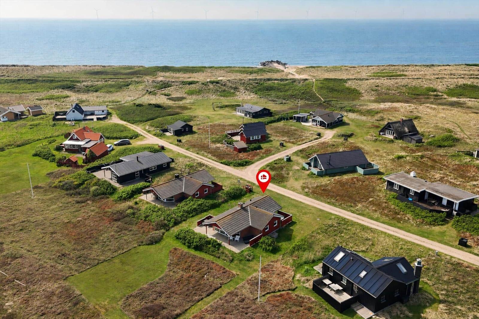 Aerial view of coastal village with houses and beach. Red marker indicates property location.