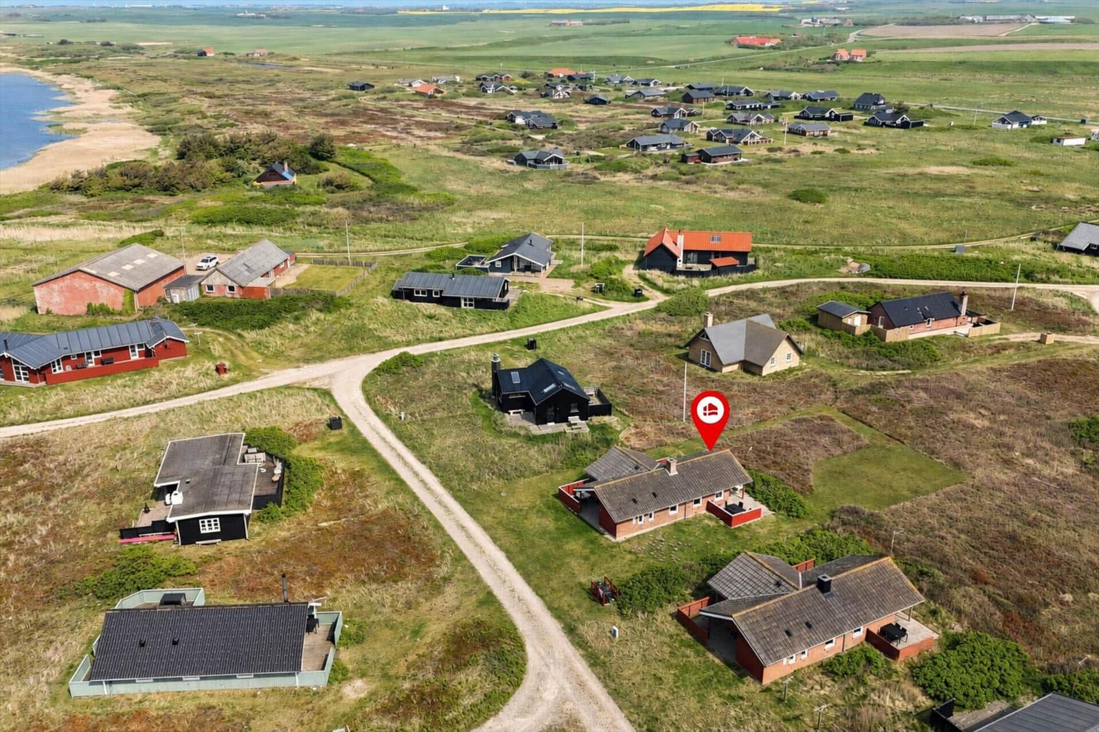 Aerial view of coastal vacation homes with grassy dunes and ocean in background.