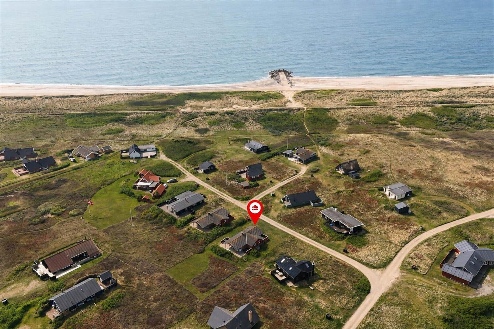 Haus mit Blick auf Meer und Strand, umgeben von Wiesen und weiteren Häusern.