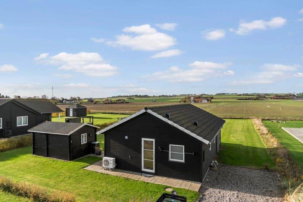 Schwarze Holzhütte mit Terrasse und Garten. Weitläufige Landschaft im Hintergrund.