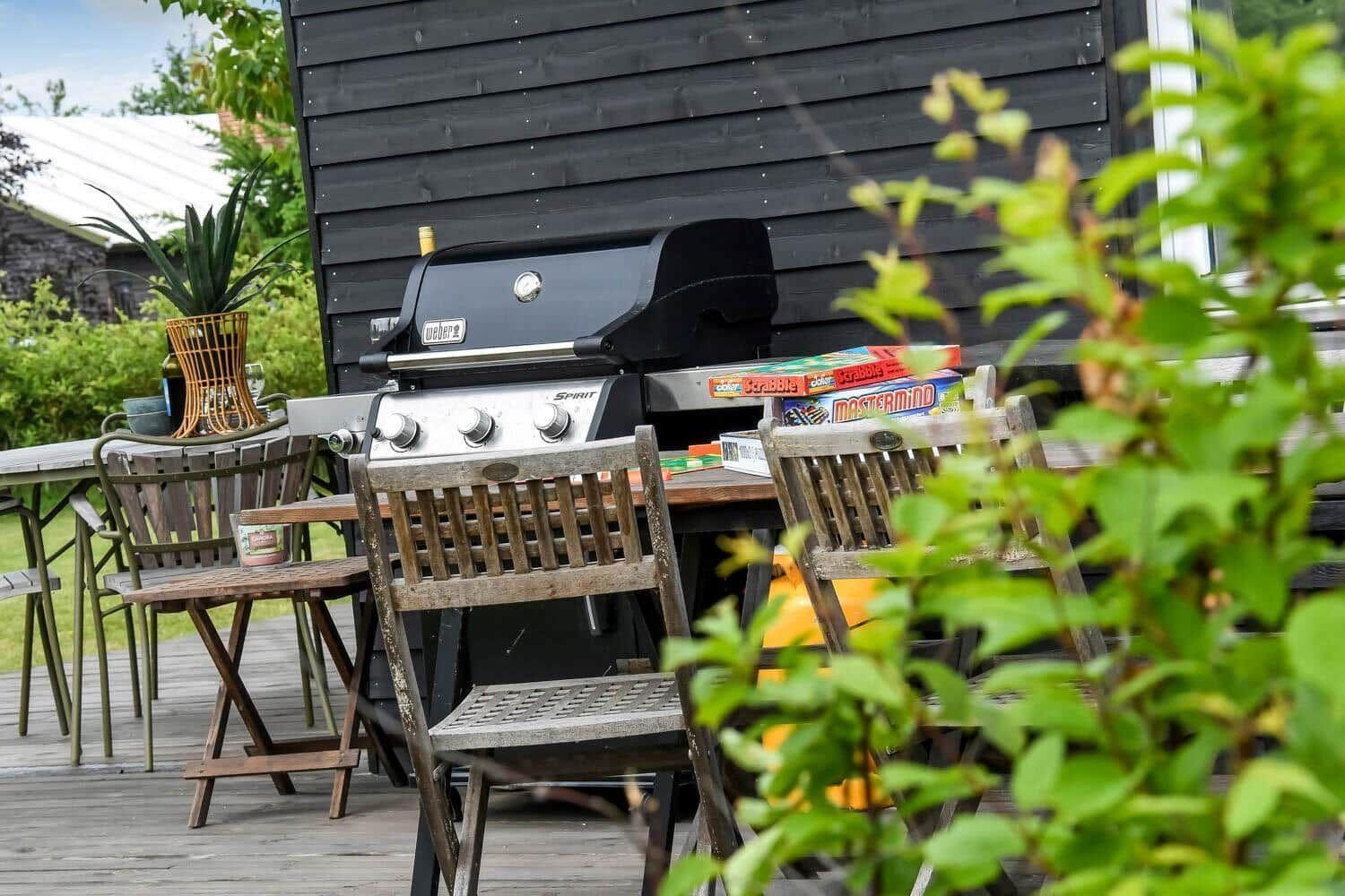 Moderne Holzhütte mit Terrasse und Garten. Gedeckter Außenbereich mit Tisch und Stühlen.